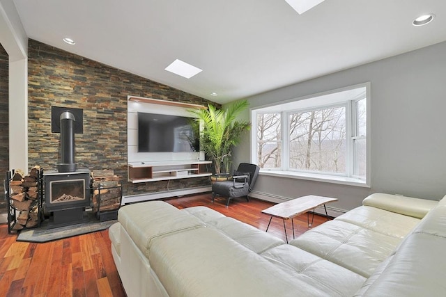 living room with a baseboard heating unit, vaulted ceiling with skylight, a wood stove, and wood-type flooring