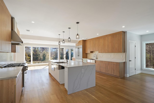 kitchen with pendant lighting, modern cabinets, high quality appliances, a large island with sink, and wall chimney exhaust hood