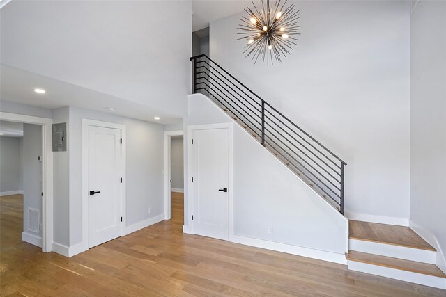 staircase with a towering ceiling, an inviting chandelier, baseboards, and wood finished floors