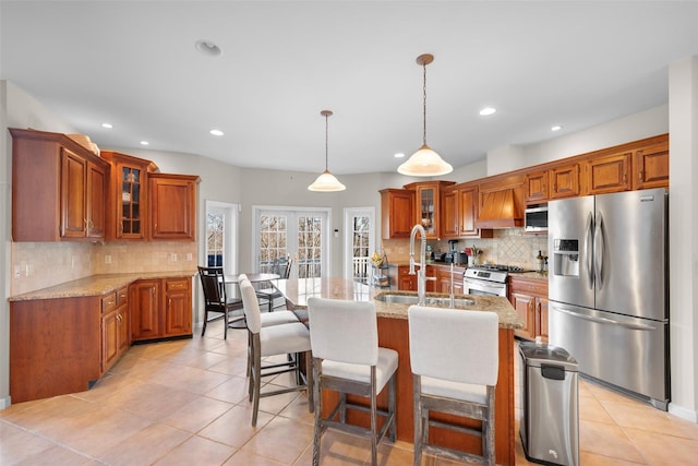 kitchen featuring sink, stainless steel appliances, a kitchen island with sink, and light stone counters