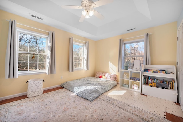 bedroom with a raised ceiling, hardwood / wood-style flooring, ceiling fan, and multiple windows