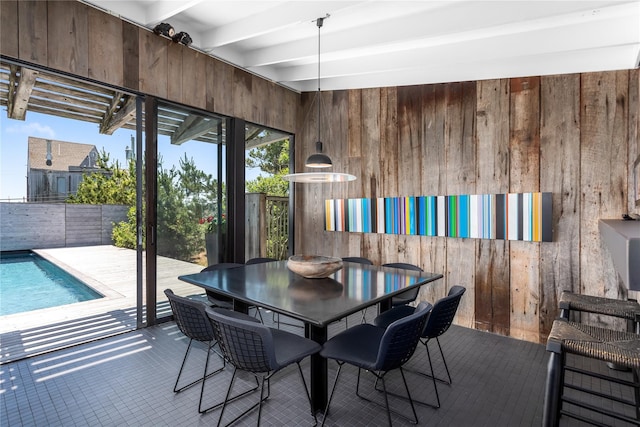 dining space featuring tile patterned flooring, beamed ceiling, and wood walls