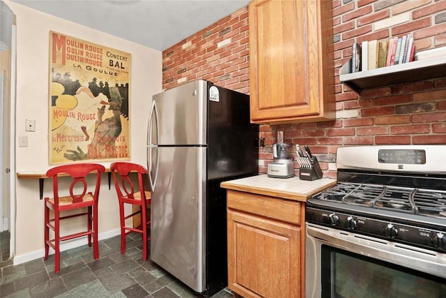 kitchen with tile counters, brick wall, and appliances with stainless steel finishes