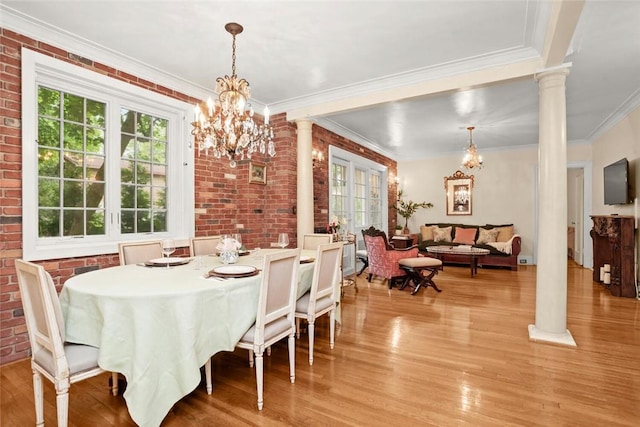 dining room with brick wall, ornate columns, a notable chandelier, and crown molding