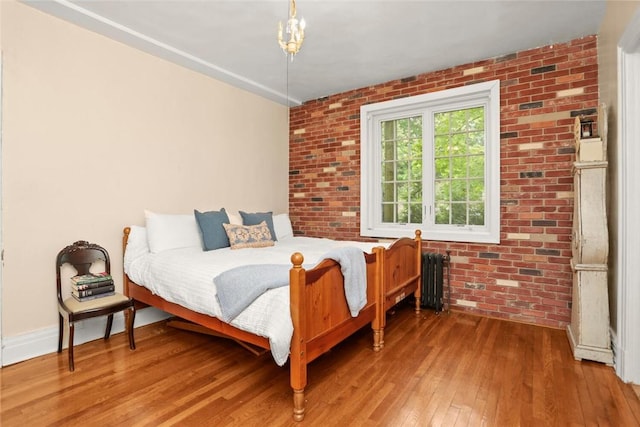 bedroom with wood-type flooring, radiator, and brick wall