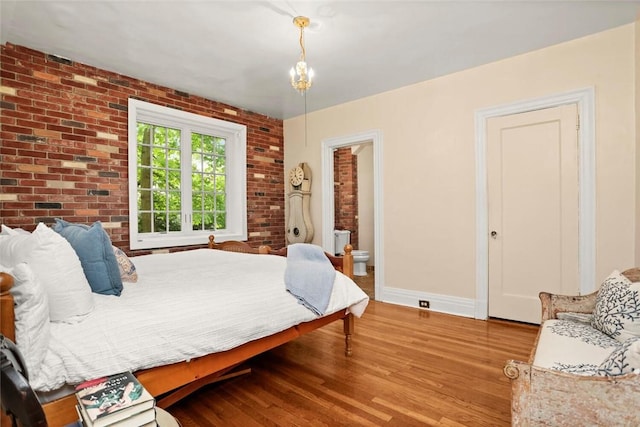 bedroom featuring ensuite bathroom, brick wall, and light hardwood / wood-style flooring