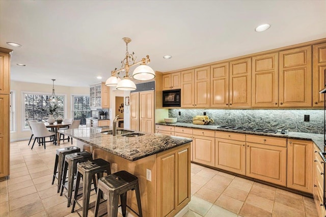 kitchen featuring pendant lighting, a kitchen island with sink, dark stone countertops, black microwave, and stainless steel gas cooktop