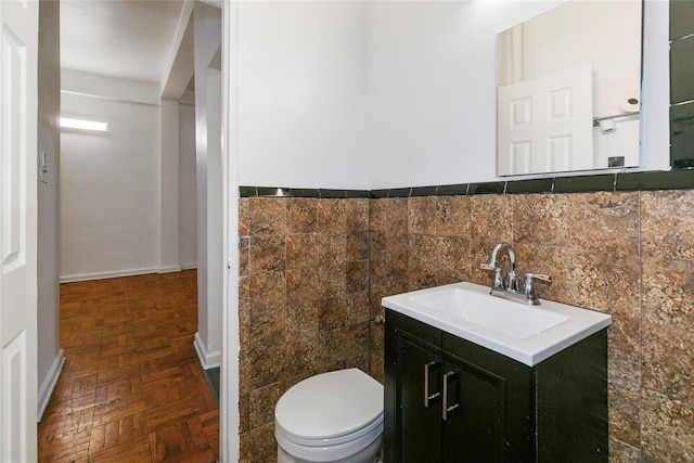 bathroom featuring toilet, tile walls, vanity, and parquet flooring