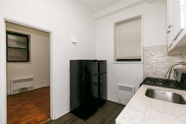 kitchen featuring white cabinets, sink, radiator heating unit, and black fridge