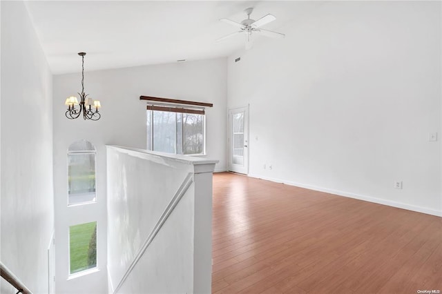 interior space featuring ceiling fan with notable chandelier, high vaulted ceiling, light wood-type flooring, and baseboards