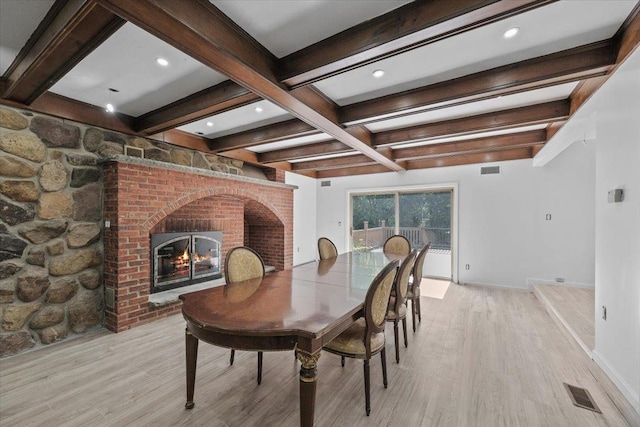 dining area featuring a fireplace, beamed ceiling, and light hardwood / wood-style flooring