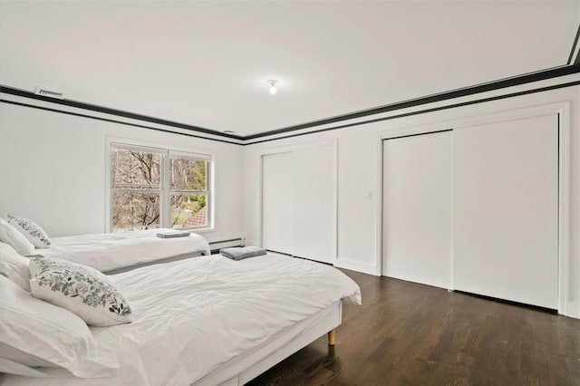 bedroom with dark hardwood / wood-style floors, crown molding, and two closets