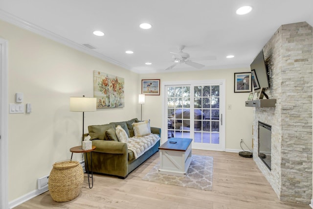 living room with crown molding, light wood-type flooring, ceiling fan, and a stone fireplace