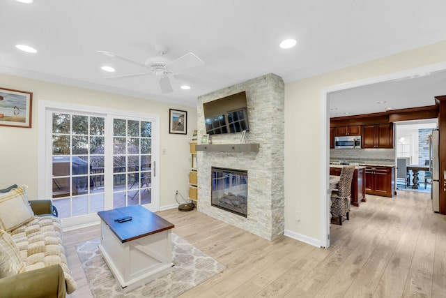 living room featuring ceiling fan, light hardwood / wood-style flooring, and a stone fireplace