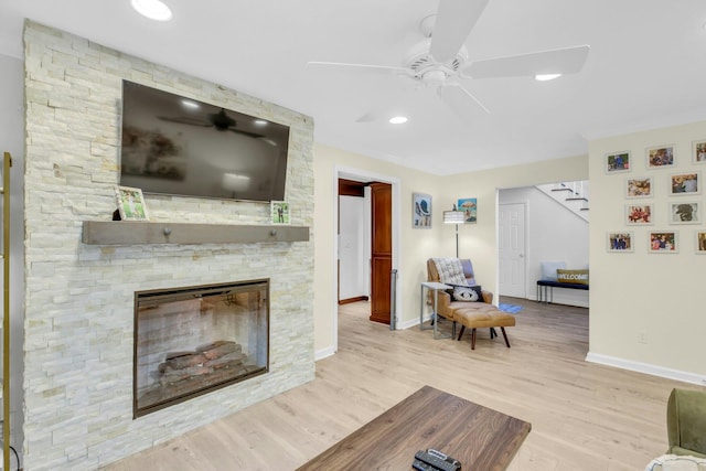 living room with ceiling fan, light hardwood / wood-style floors, and a stone fireplace