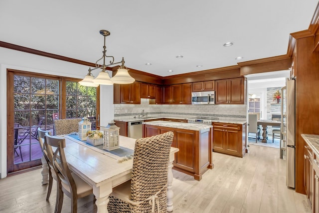 kitchen with hanging light fixtures, light wood-type flooring, a center island, ornamental molding, and stainless steel appliances