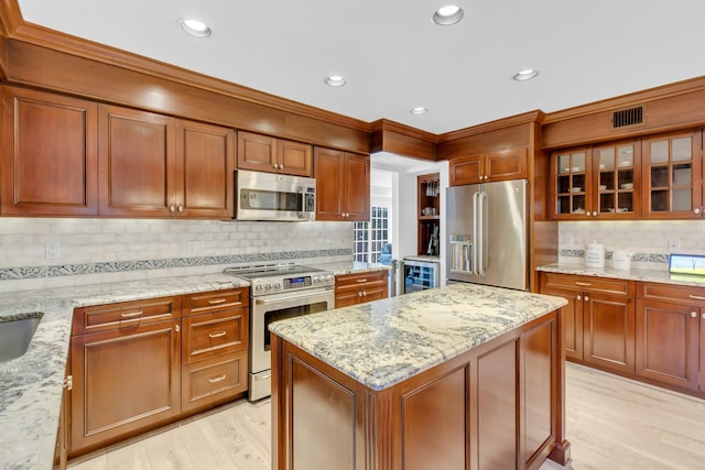 kitchen with appliances with stainless steel finishes, light wood-type flooring, light stone countertops, a kitchen island, and beverage cooler