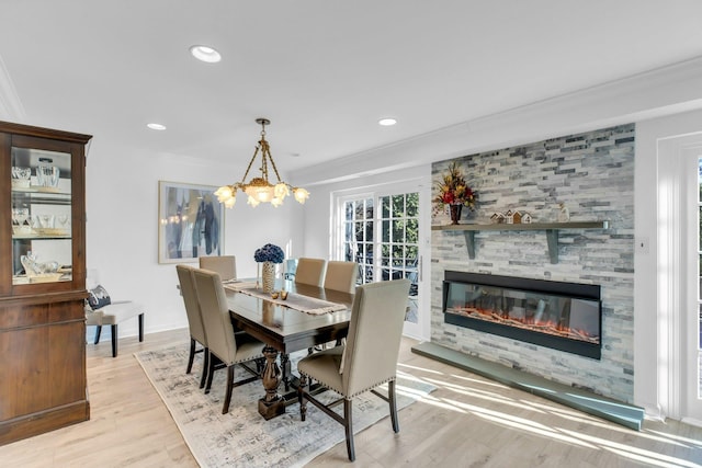 dining space with crown molding, a tiled fireplace, light hardwood / wood-style floors, and a notable chandelier