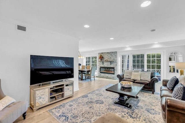 living room with a notable chandelier, crown molding, a stone fireplace, and light wood-type flooring