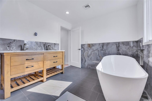 bathroom with tile patterned floors, tile walls, a bathing tub, and sink