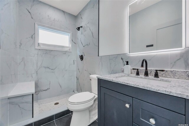 bathroom with a tile shower, vanity, tile walls, tile patterned flooring, and toilet