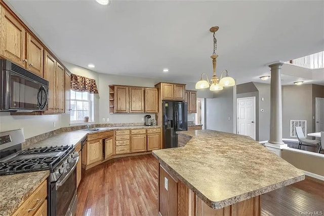 kitchen featuring ornate columns, hanging light fixtures, a notable chandelier, a kitchen island, and black appliances