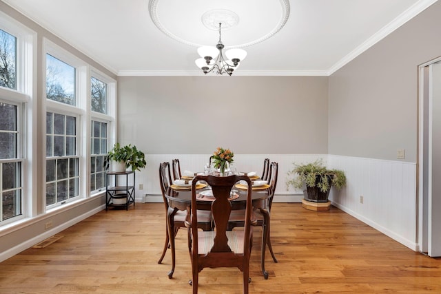 dining space with an inviting chandelier, ornamental molding, light hardwood / wood-style flooring, and a wealth of natural light