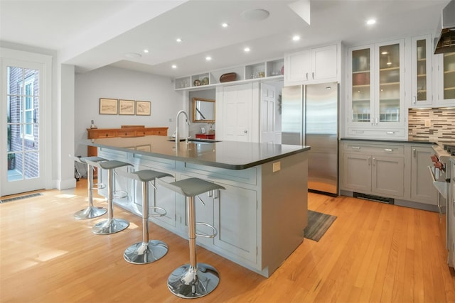 kitchen featuring an island with sink, tasteful backsplash, gray cabinets, stainless steel refrigerator, and a breakfast bar area