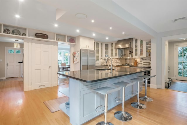 kitchen with white cabinetry, plenty of natural light, wall chimney range hood, stainless steel built in refrigerator, and sink