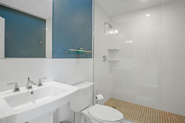 bathroom featuring tasteful backsplash, sink, tile walls, toilet, and a tile shower