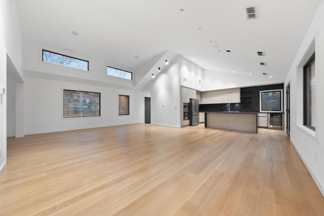 unfurnished living room with light hardwood / wood-style flooring, high vaulted ceiling, and beverage cooler