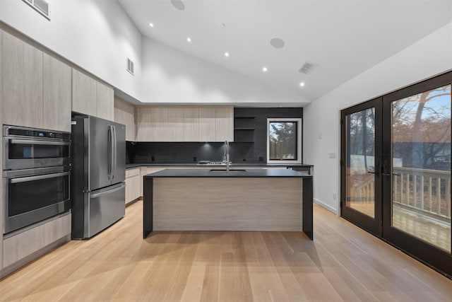 kitchen featuring sink, stainless steel appliances, light hardwood / wood-style floors, a center island with sink, and french doors