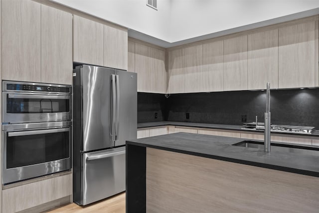 kitchen with tasteful backsplash, appliances with stainless steel finishes, light brown cabinetry, and light hardwood / wood-style flooring