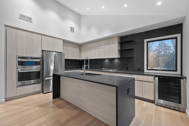 kitchen with sink, a kitchen island with sink, stainless steel appliances, wine cooler, and light hardwood / wood-style floors