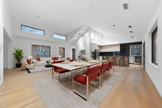 dining space with wine cooler, a towering ceiling, and light wood-type flooring