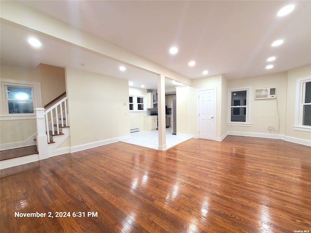 basement with hardwood / wood-style flooring, an AC wall unit, baseboard heating, and stainless steel refrigerator