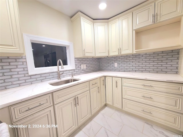 kitchen featuring cream cabinetry, decorative backsplash, light stone counters, and sink