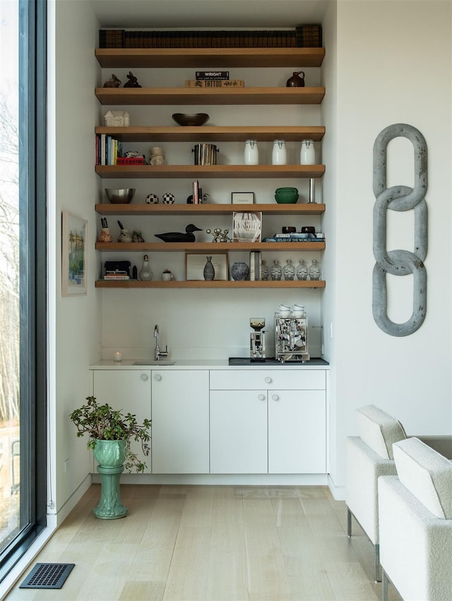 bar with white cabinetry, sink, and light wood-type flooring