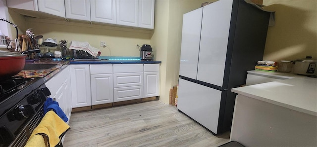 kitchen with white cabinets, black gas stove, light wood-type flooring, and white refrigerator