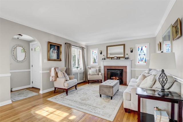 living room with a healthy amount of sunlight, crown molding, light hardwood / wood-style floors, and a brick fireplace