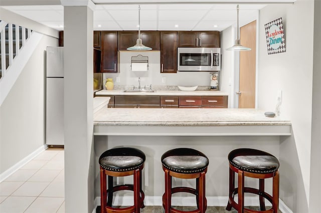 kitchen with a breakfast bar area, light stone counters, sink, and hanging light fixtures