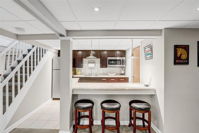 kitchen with a breakfast bar, white fridge, a drop ceiling, and sink