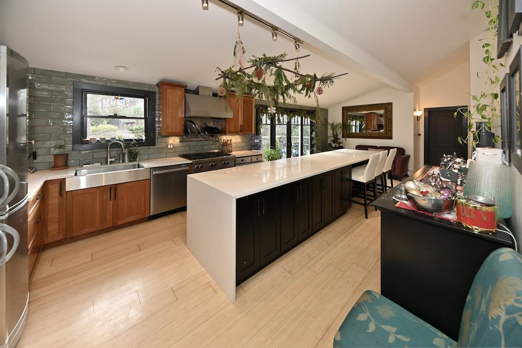 kitchen with decorative backsplash, appliances with stainless steel finishes, sink, wall chimney range hood, and a kitchen island