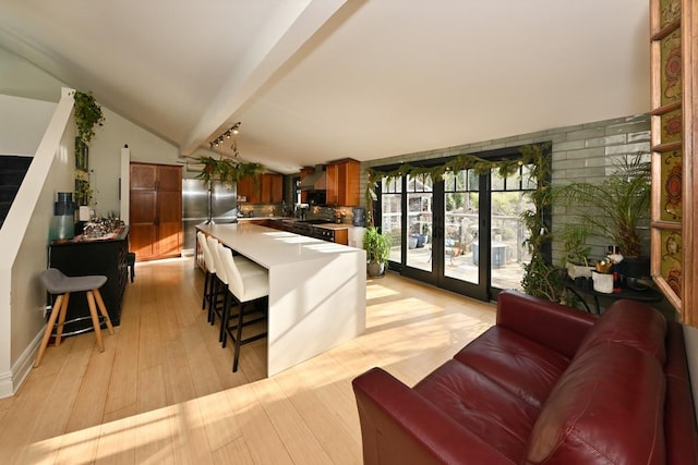 kitchen featuring stainless steel refrigerator, french doors, light hardwood / wood-style flooring, lofted ceiling with beams, and a breakfast bar