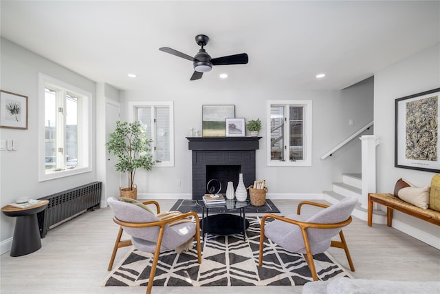 living room with a fireplace, ceiling fan, radiator heating unit, and light hardwood / wood-style flooring