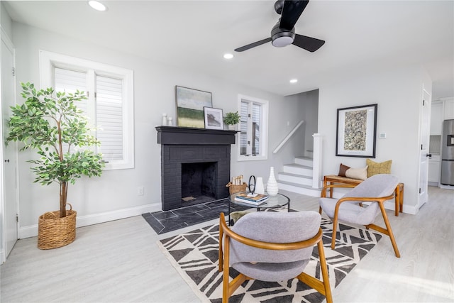 living room featuring ceiling fan, light hardwood / wood-style flooring, and a brick fireplace