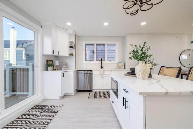 kitchen featuring dishwasher, a breakfast bar, built in microwave, light stone counters, and white cabinetry