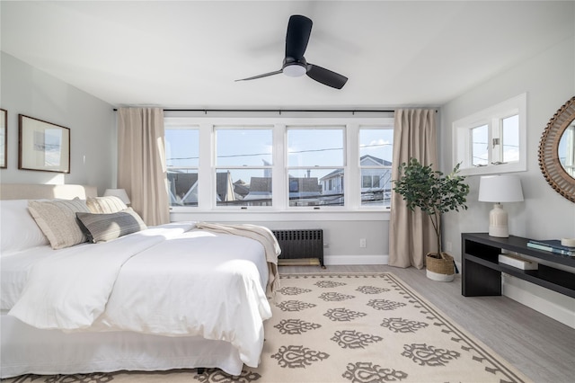 bedroom featuring multiple windows, ceiling fan, radiator heating unit, and light hardwood / wood-style flooring