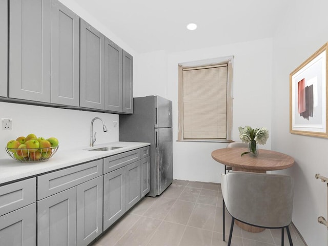 kitchen with stainless steel fridge, light tile patterned floors, gray cabinetry, and sink