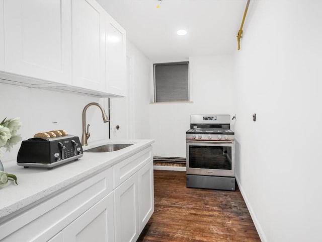 kitchen with dark wood-type flooring, stainless steel range with gas cooktop, sink, light stone countertops, and white cabinetry